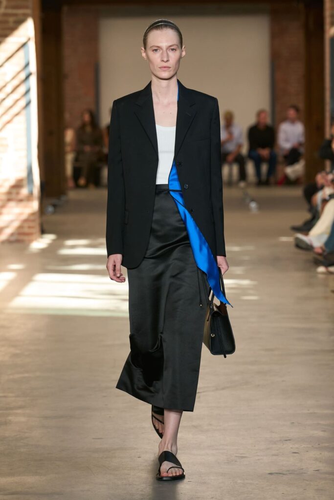 Look Calvin Klein Collection primavera 2027 con blazer nero, gonna in raso e accento blu royal