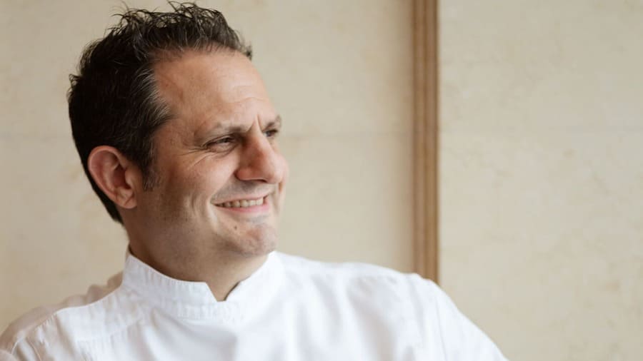 Guillaume Galliot, chef di Caprice a Hong Kong, sorride in un ritratto con la giacca bianca da cucina.