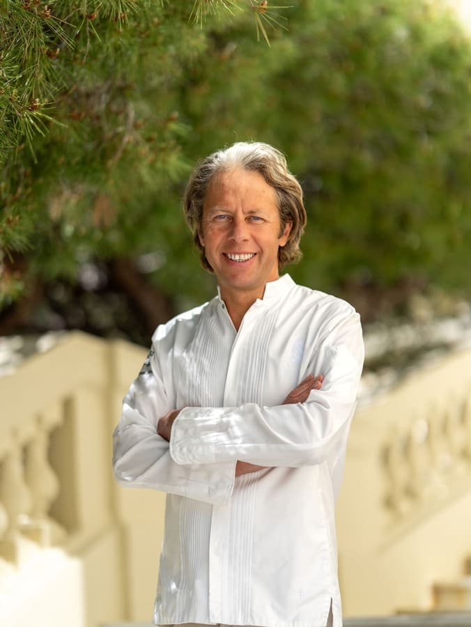 Yoric Tièche, chef di Le Cap a Cap-Ferrat, ritratto all’aperto in giacca bianca tra alberi e vegetazione.
