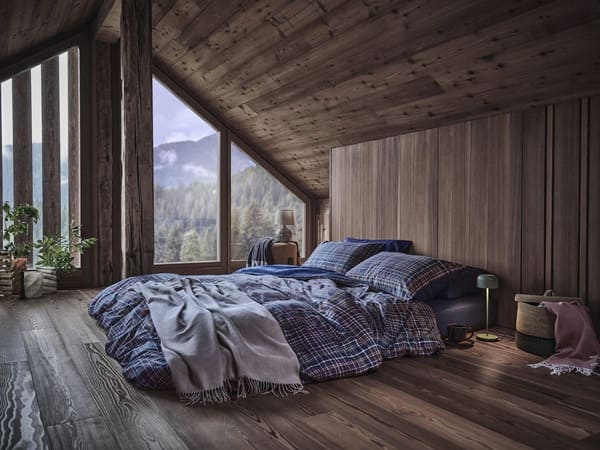 Camera da letto con biancheria a quadri della collezione Coincasa Abitare la natura, in un ambiente in legno