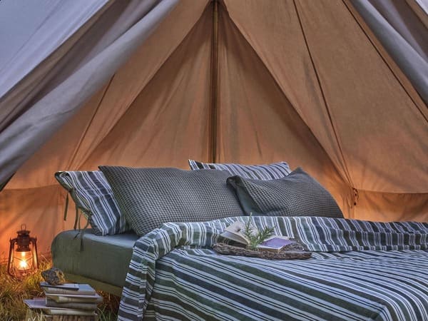Biancheria da letto a righe della collezione Coincasa Abitare la natura allestita in una tenda