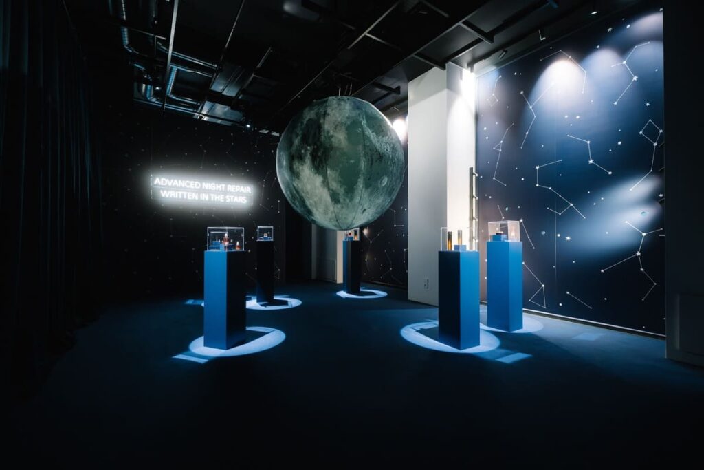 Sala immersiva del pop-up Estée Lauder "Written in the Stars" a Milano, con una grande sfera a forma di luna e pareti a tema costellazioni