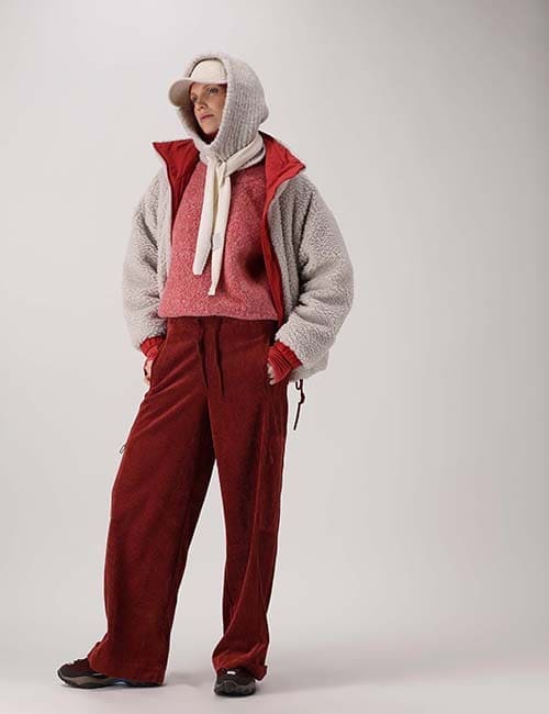 Modella su fondo chiaro con cappuccio grigio, abbinamento grigio e rosso e mani nelle tasche.