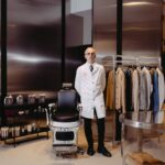 Maurizio Prota nella boutique PT Torino di Milano, accanto a una poltrona da barbiere e alle Colonie 1904 di Antica Barbieria Colla.