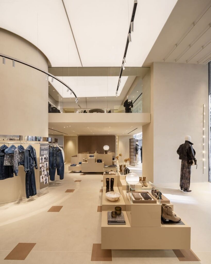 Sala Liu Jo a Milano con tavoli espositivi centrali, capi in denim a sinistra e mezzanino sul fondo.