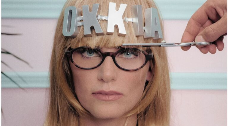 Modella con occhiali da lettura OKKIA Lucca in effetto havana e le lettere del logo OKKIA applicate ai capelli, in un'immagine della campagna del brand ambientata in un salone di bellezza