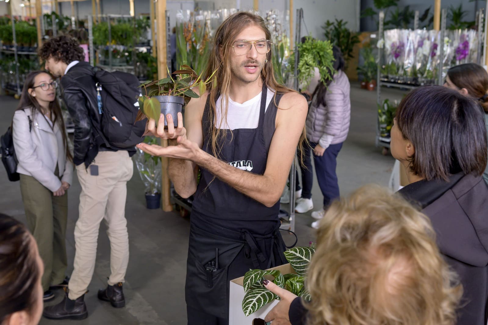 Un membro dello staff Piantala mostra una pianta a un gruppo di visitatori tra gli scaffali del pop-up