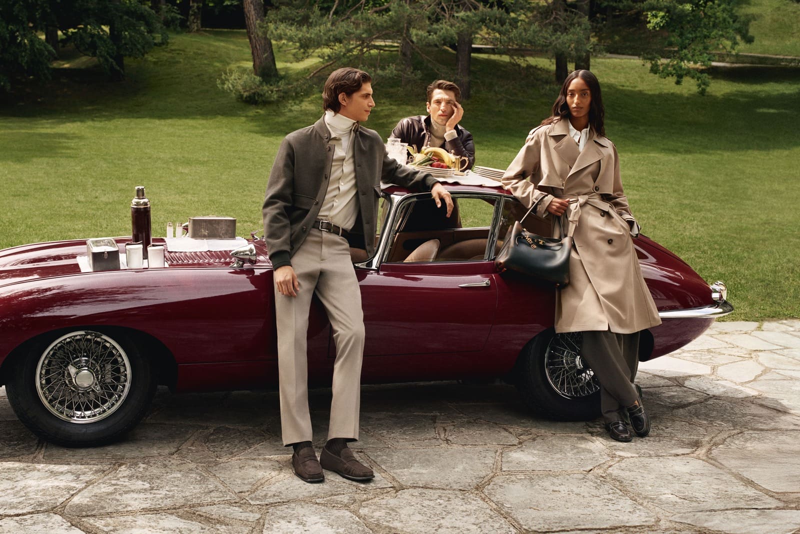 Modelli della campagna Tod's autunno inverno 2026-27 con auto d'epoca nel parco di Villa San Martino, uno con borsa nera a doppio manico