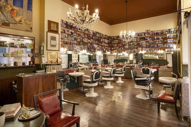 Interno della bottega storica Antica Barbieria Colla a Milano, con poltrone da barbiere, specchi e pareti ricoperte di fotografie.