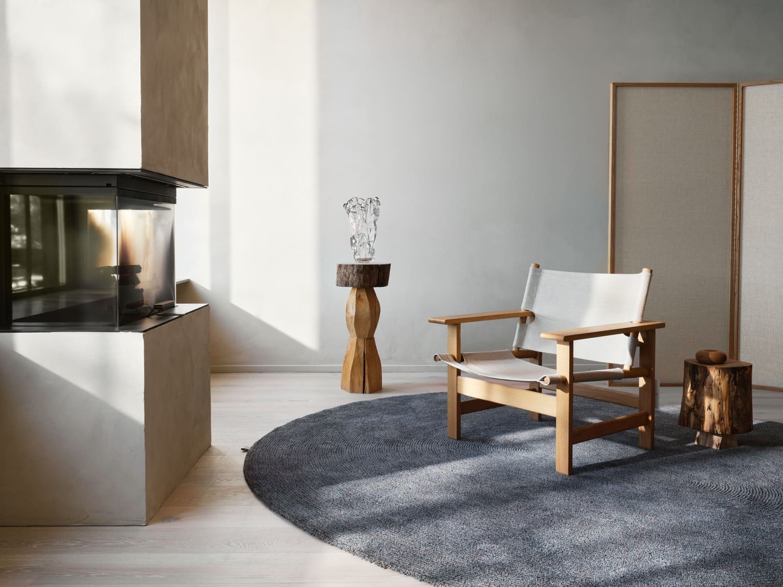 Tappeto ovale Spire Oval della collezione Landskab di Kasthall nella colorazione Malm, in un living con camino e poltrona in legno